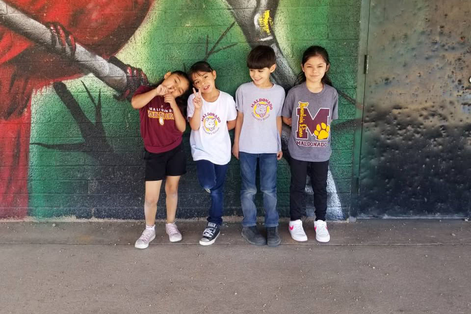 Four students wear their school spirit wear in front of a mural