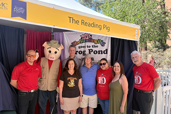 A group of people and a pig mascot stand under a tent at the Festival of Books