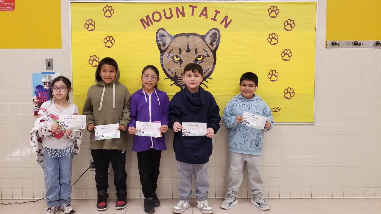 Five students hold up awards certificates in front of a yellow banner with Mountain Lions written on it and a mountain lion head