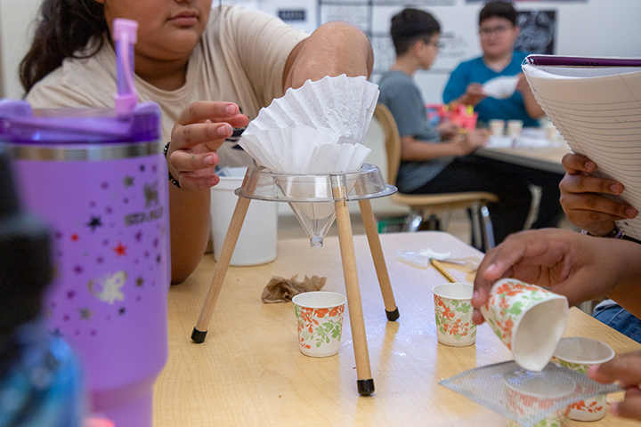 A girl reaches her hand into a coffee filter funnel