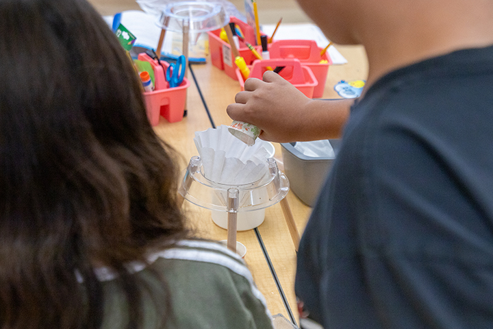 A boy pours a cup into a coffee filter