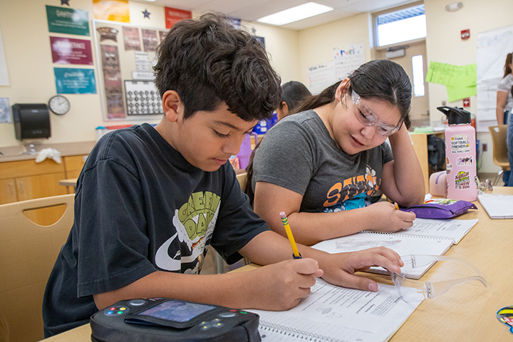 A boy and girl write down notes about their science experiment