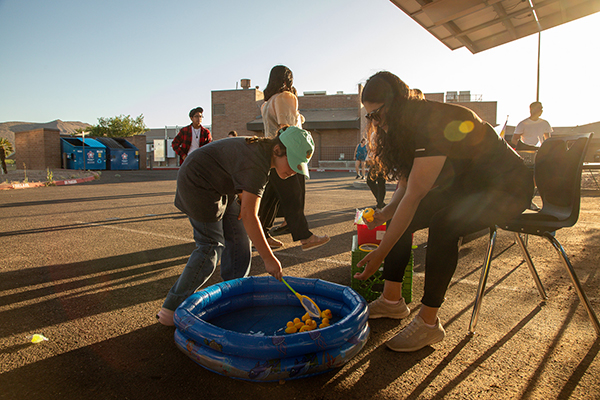 A woman helps a girl as she tries to scoop rubber ducks out of a baby pool