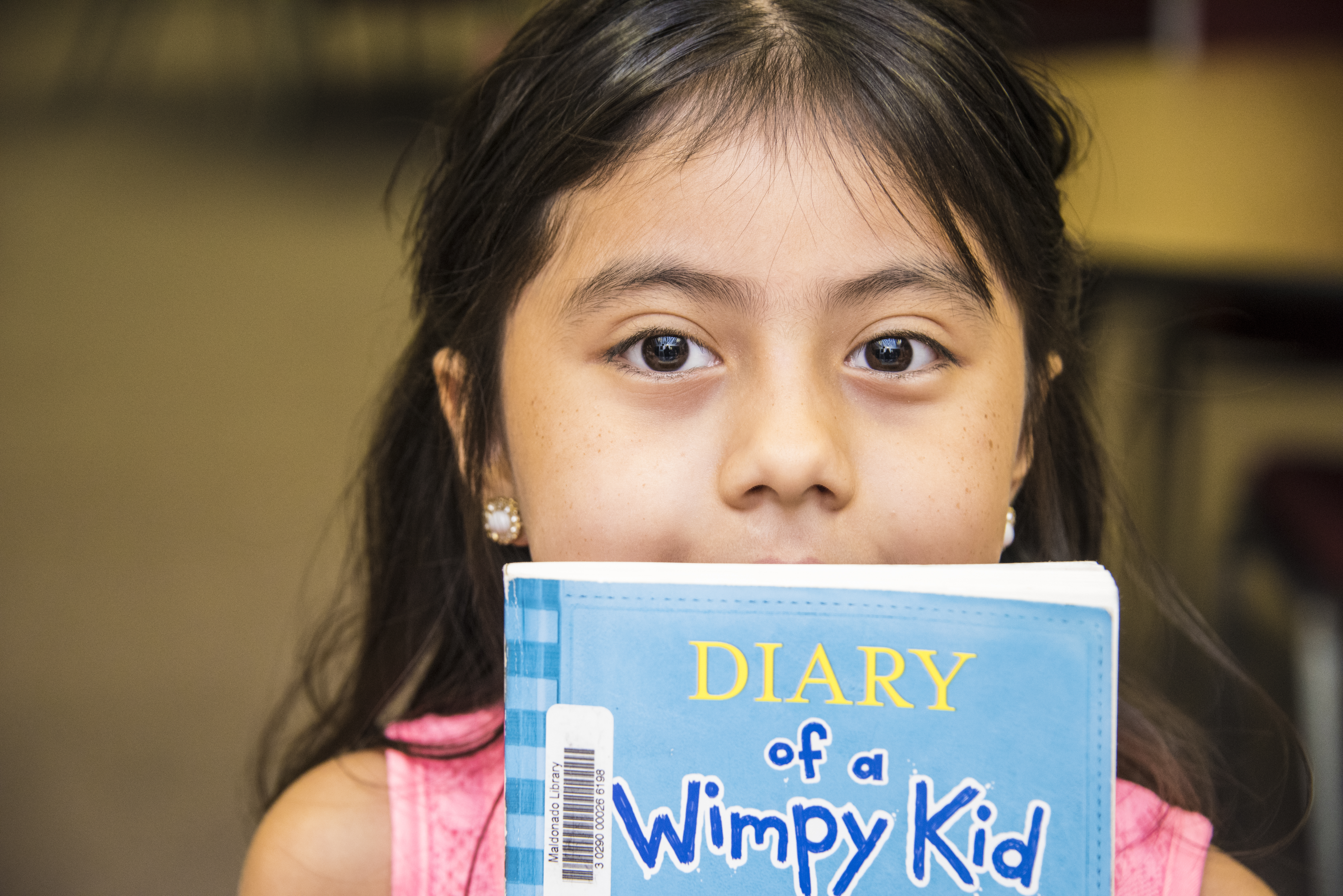 A little girl holds a Diary of a Wimpy Kid book in front of her face